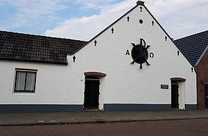 Op de foto is een wit kerkgebouw te zien met een zwarte klok op de gevel