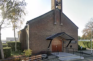 Op de foto is een bruin kerkgebouw met bomen te zien
