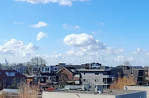 Op de foto zijn meerdere daken en een blauwe lucht te zien.