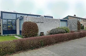 Op de foto is een gebouw te zien met struiken en een lichtdonkere lucht.